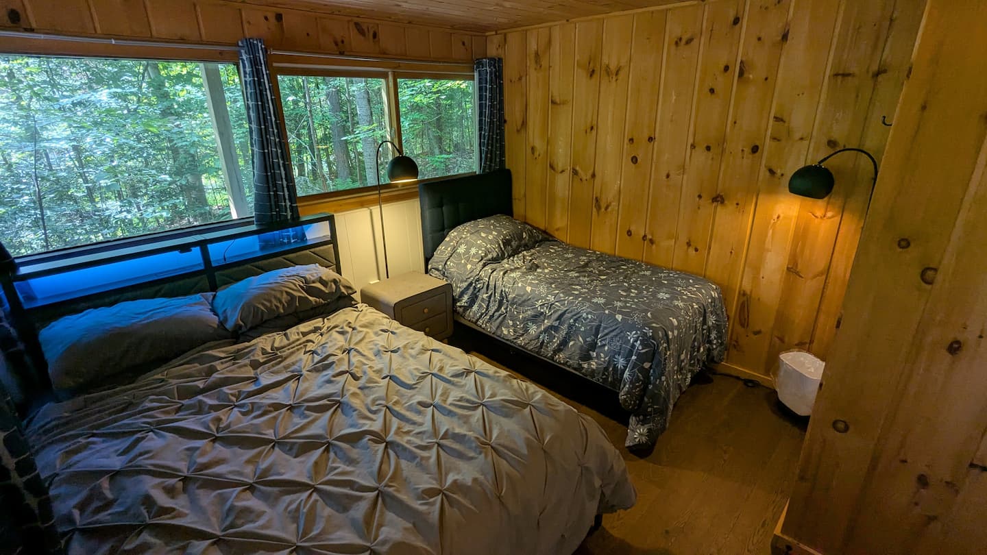 Bedroom with wrap-around forest windows, a queen bed, and a twin bed