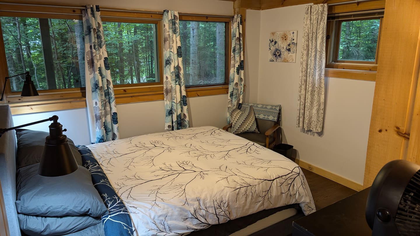 Bedroom with a queen bed, floral curtains, and windows looking into the woods