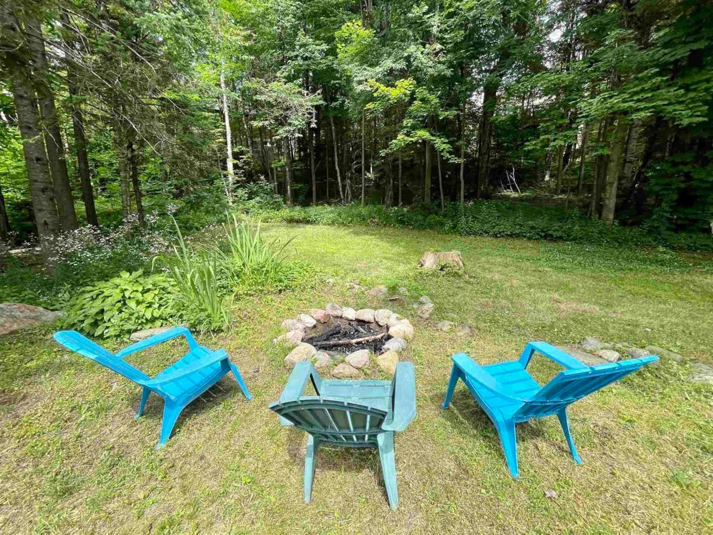 Stone fire pit in the woods with three Adirondack chairs