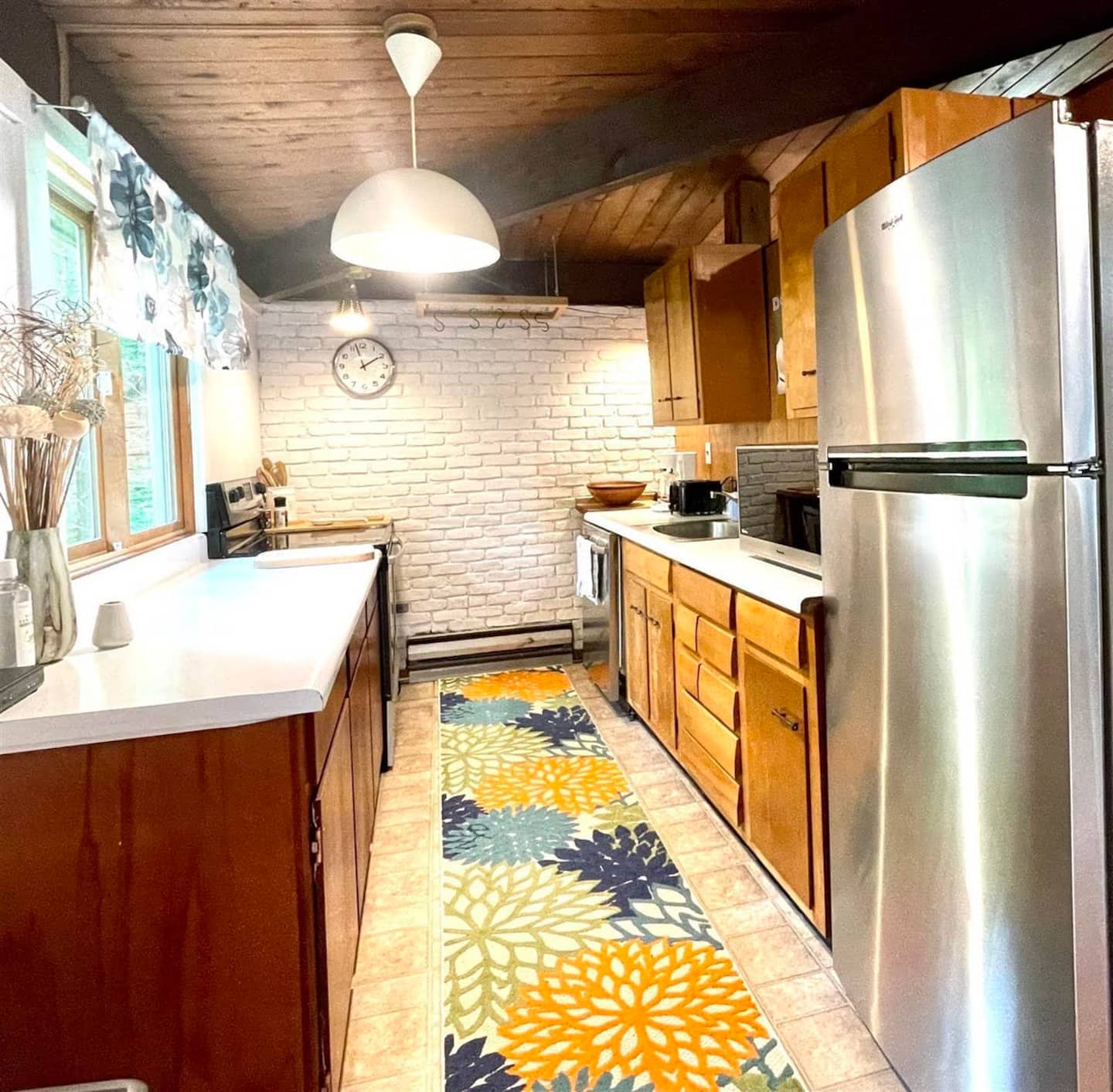 Galley kitchen with wood cabinets, a white brick wall, and a colorful runner